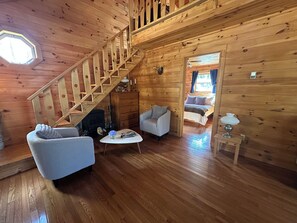 A wooden interior with a staircase, a fireplace, two sofas, a coffee table, and a bed.