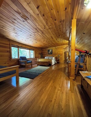 Interior de una cabaña con paredes y suelos de madera, una cama, un escritorio y una silla.