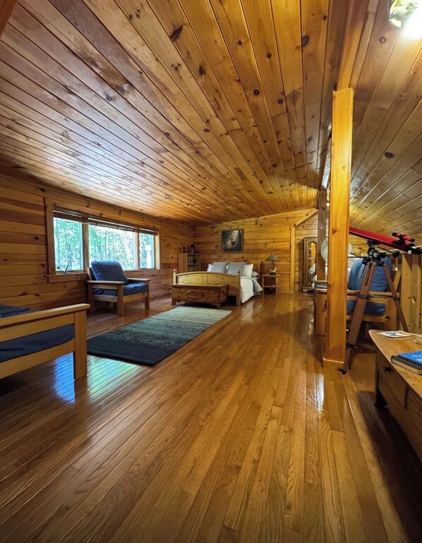A cabin interior with wooden walls and floors, a bed, a desk, and a chair.