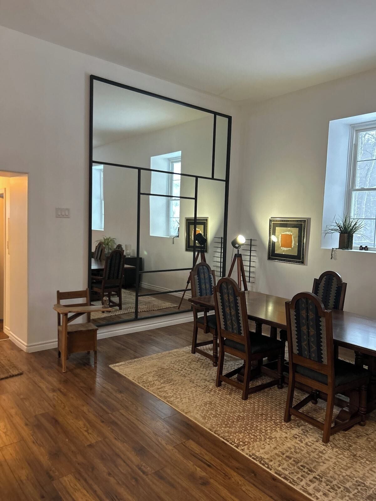 A dining area with a wooden table and chairs, a rug, and a large mirror on the wall.