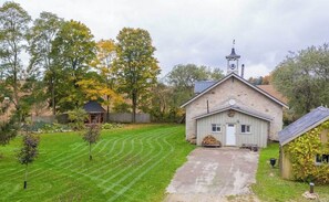 En byggnad av sten med ett klocktorn, omgiven av en välskött gräsmatta och träd.