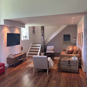 A modern living room with a staircase, a flat-screen TV, and a comfortable seating area.
