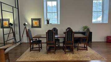 A dining area with a wooden table and chairs, two windows, and a red cooler.