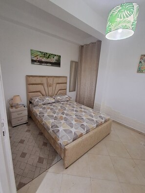A bedroom with a bed, a nightstand, a lamp, a painting, and a green patterned light fixture. - Vrbo Property (Tanger)