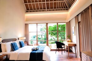 A hotel room with a bed, bedside table, chair, desk, and large windows. - Ijen Resort (Banyuwangi)
