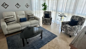 Una sala de estar con sofá, sillón, mesa de centro y una planta en maceta.