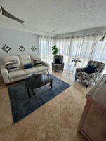 Una sala de estar con sofá, sillón, mesa de centro y una planta en maceta.