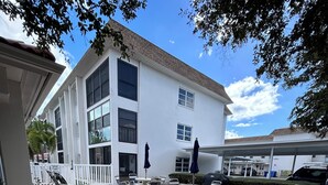 Un patio de hotel con mobiliario exterior, una zona cubierta y un edificio con varias ventanas.