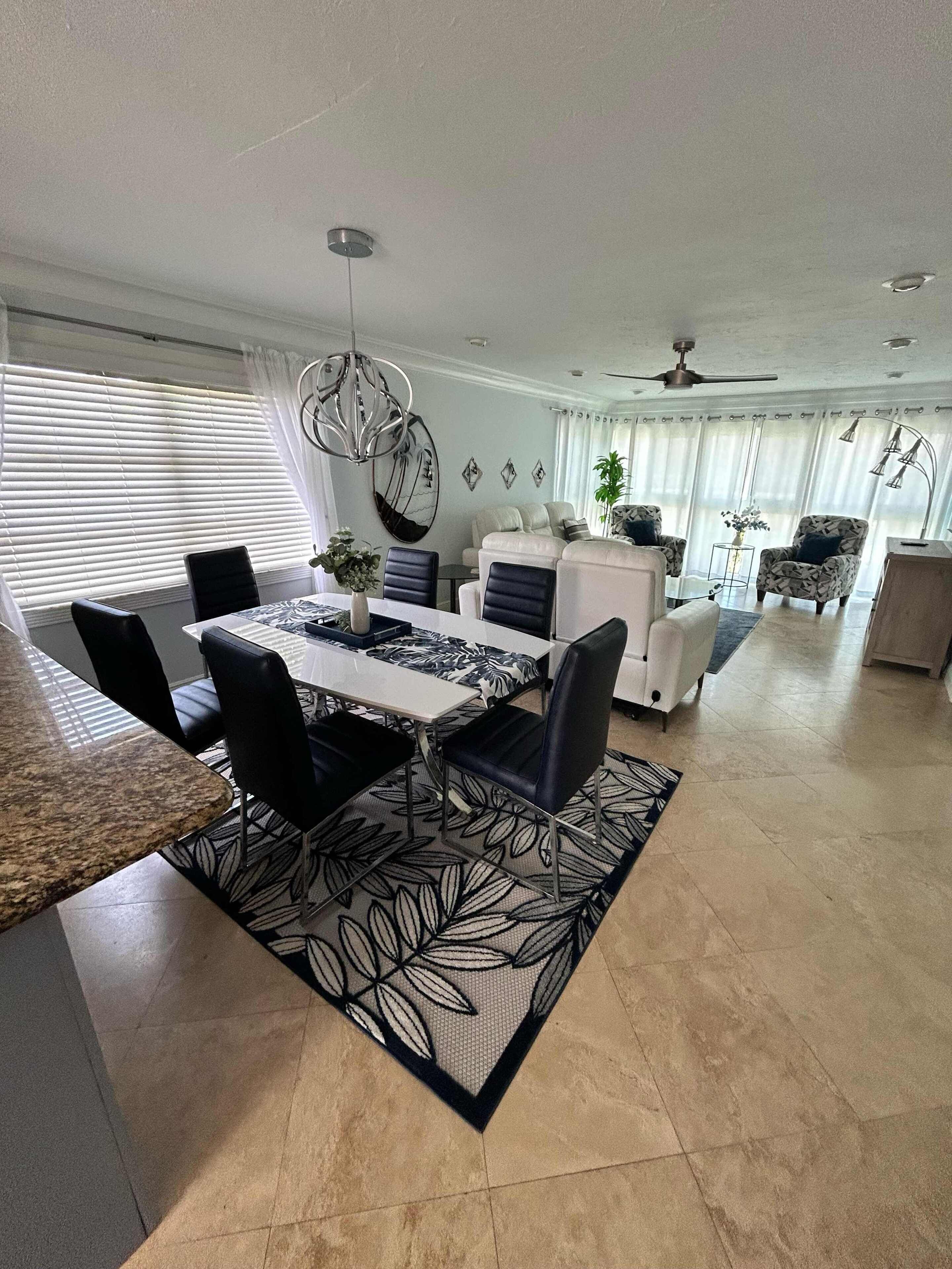 A modern dining area with a large table, chairs, and a patterned rug.