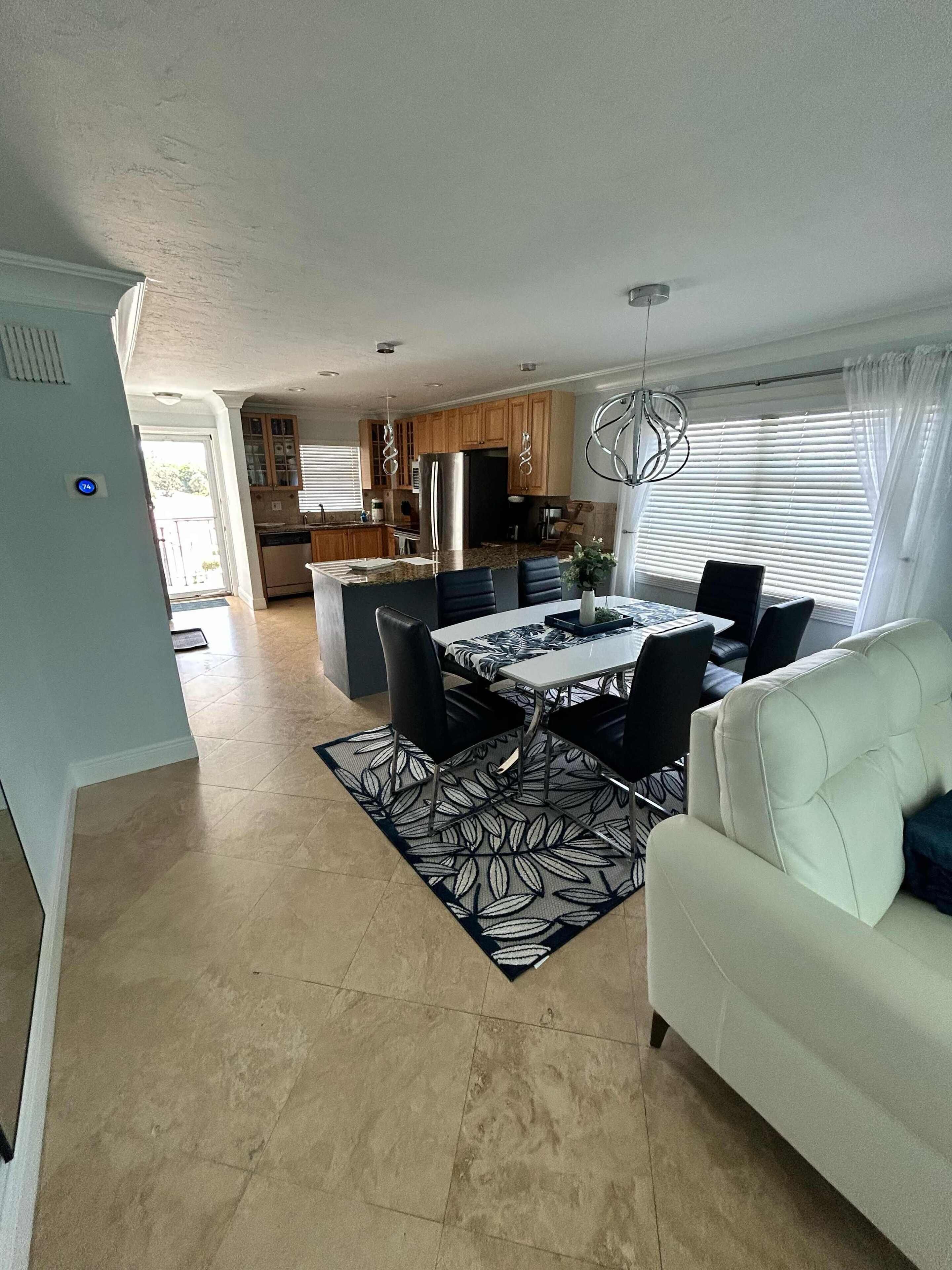 A spacious living area with a dining table, black chairs, a white sofa, and a patterned rug.