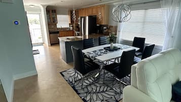 A spacious living area with a dining table, black chairs, a white sofa, and a patterned rug.