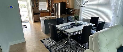 A spacious living area with a dining table, black chairs, a white sofa, and a patterned rug.