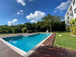 A rectangular swimming pool with a clear blue water surface, surrounded by a brick walkway and lush greenery. - Enchanting 1-bedroom condo with AC in vibrant Freeport (Freeport)