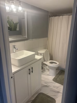 A bathroom with a white sink, a toilet, and a shower curtain. - Enchanting 1-bedroom condo with AC in vibrant Freeport (Freeport)
