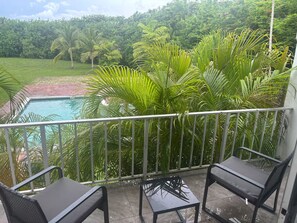 Ein Balkon mit zwei Stühlen, einem kleinen Tisch und Blick auf einen Pool, der von üppiger Vegetation umgeben ist.