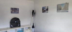A room with a white wall, a standing fan, a white cabinet with drawers, and three framed pictures depicting winter scenes. - 2BR Frimley Home Near High Street (Camberley)