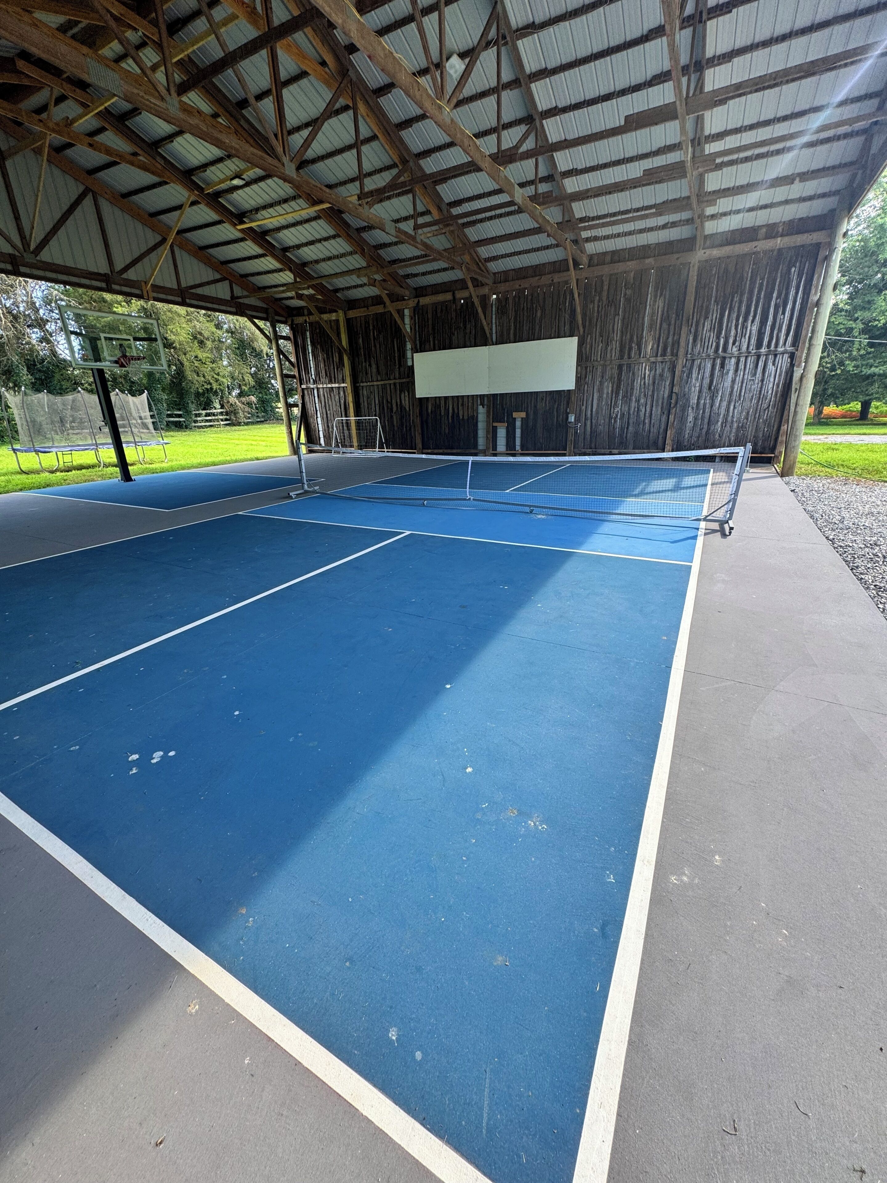 An indoor tennis court with a blue playing surface, a net, and a wooden roof structure.