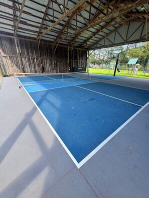Un campo da tennis all'aperto con tetto in metallo e canestro da basket.