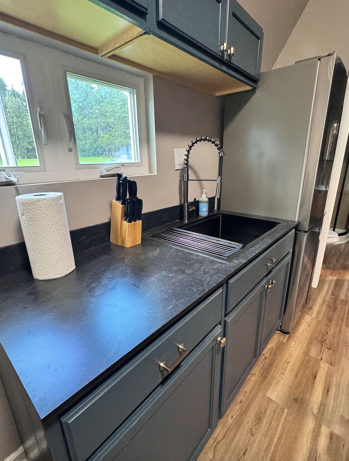 Una cocina con encimera negra, pileta de acero inoxidable y refrigerador.