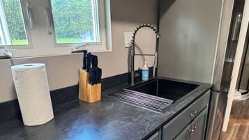 Una cocina con encimera negra, pileta de acero inoxidable y refrigerador.