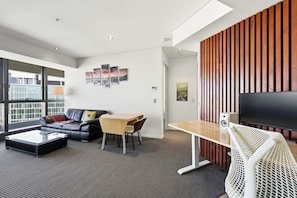 A modern living room with a sofa, coffee table, TV, and a wooden accent wall. - Brisbane Sky Retreat Views, Pool, Gym & Workspace (Brisbane City)