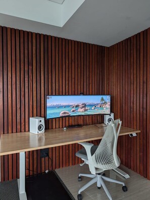 A modern office space with a wooden panel wall, a desk with a computer monitor, a white office chair, and a speaker. - Brisbane Sky Retreat Views, Pool, Gym & Workspace (Brisbane City)