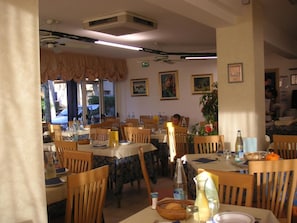 A restaurant interior with multiple tables, chairs, and a ceiling fan. - Canasta (Riccione)