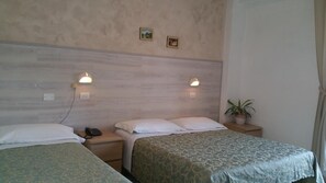 A hotel room with two beds, a wooden headboard, bedside lamps, a telephone, a potted plant, and a wall-mounted light switch. - Canasta (Riccione)