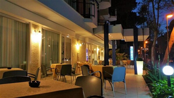 An outdoor dining area with tables and chairs, a covered seating area, and a street lamp. - Canasta (Riccione)
