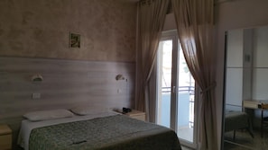 A hotel room with a bed, bedside table, a telephone, a mirror, and a view of the outside through a sliding door. - Canasta (Riccione)