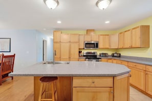 Una cocina con armarios de madera, encimera de granito, electrodomésticos de acero inoxidable y un taburete de bar.