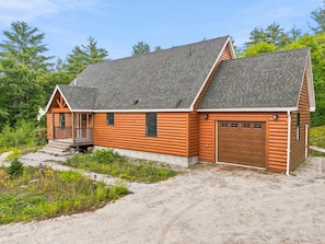 A log cabin with a porch, a garage, and a gravel driveway. - 3BR Bethel retreat with patio, fire pit, WiFi, grill and parking. (Bethel)