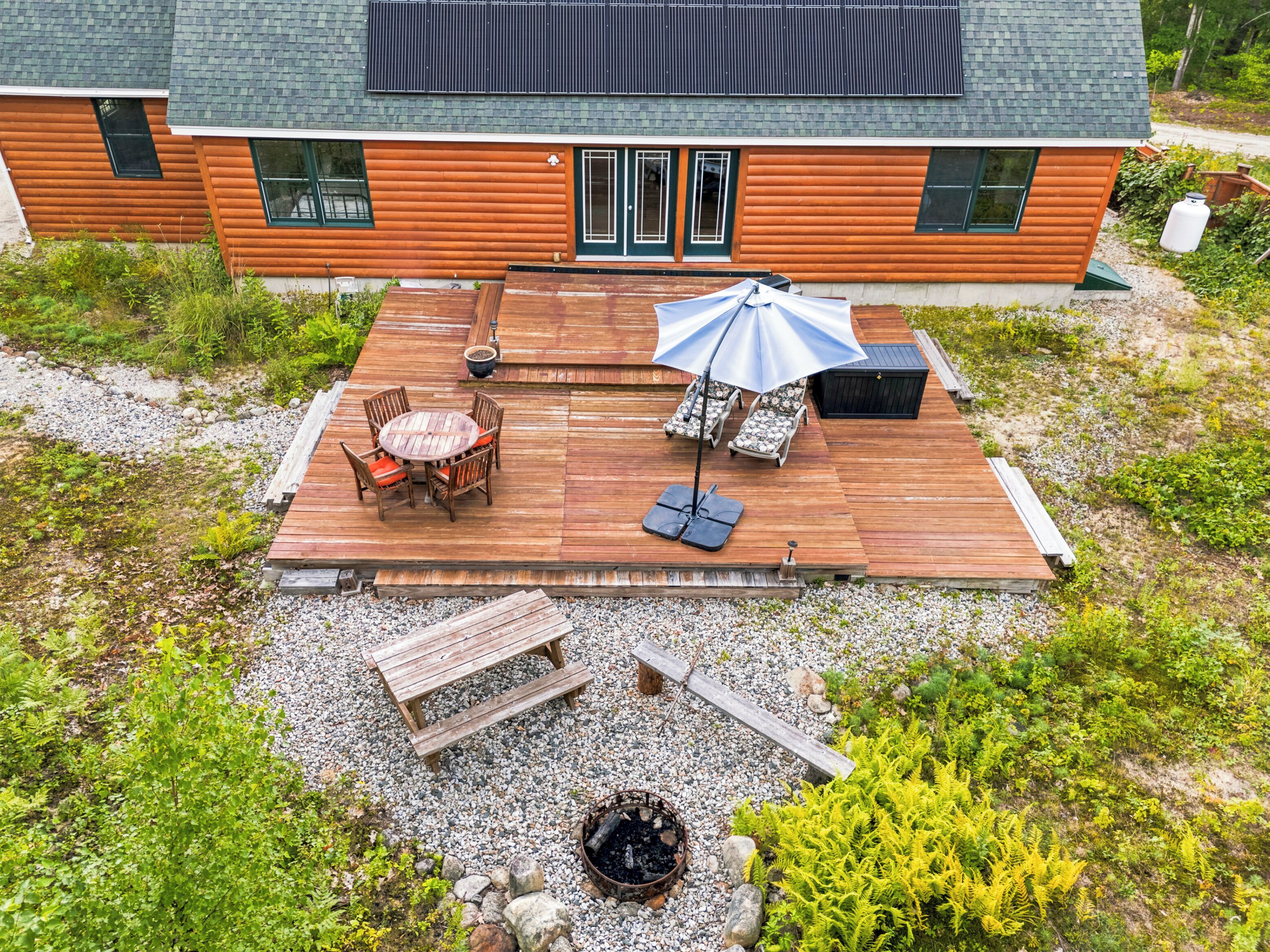 A wooden deck with a table and chairs, a lounge chair with an umbrella, a hot tub, and a fire pit.