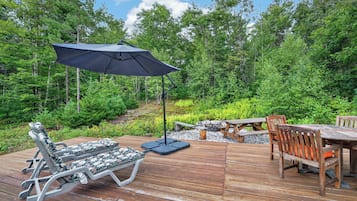 A wooden deck with a lounge chair, a table with chairs, and a large umbrella.