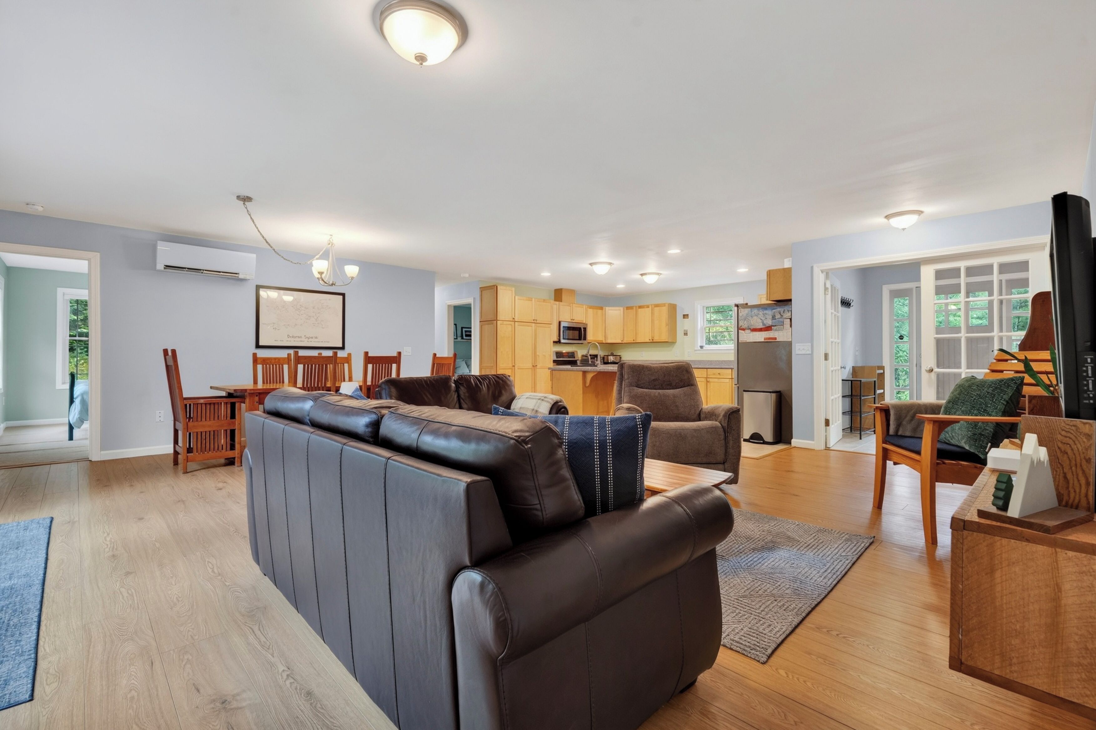 A modern living room with a leather sofa, wooden dining table, and a kitchen area with wooden cabinets and a microwave.