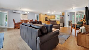 Una sala de estar moderna con un sofá de cuero, una mesa de comedor de madera y una zona de cocina con armarios de madera y un microondas.