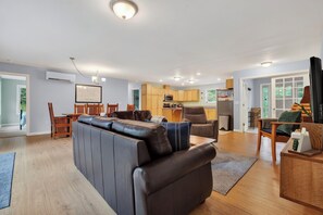 A modern living room with a leather sofa, wooden dining table, and a kitchen area with wooden cabinets and a microwave. - 3BR Bethel retreat with patio, fire pit, WiFi, grill and parking. (Bethel)