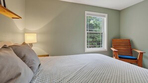 Un dormitorio con cama, una silla, un ventanal y una lámpara.