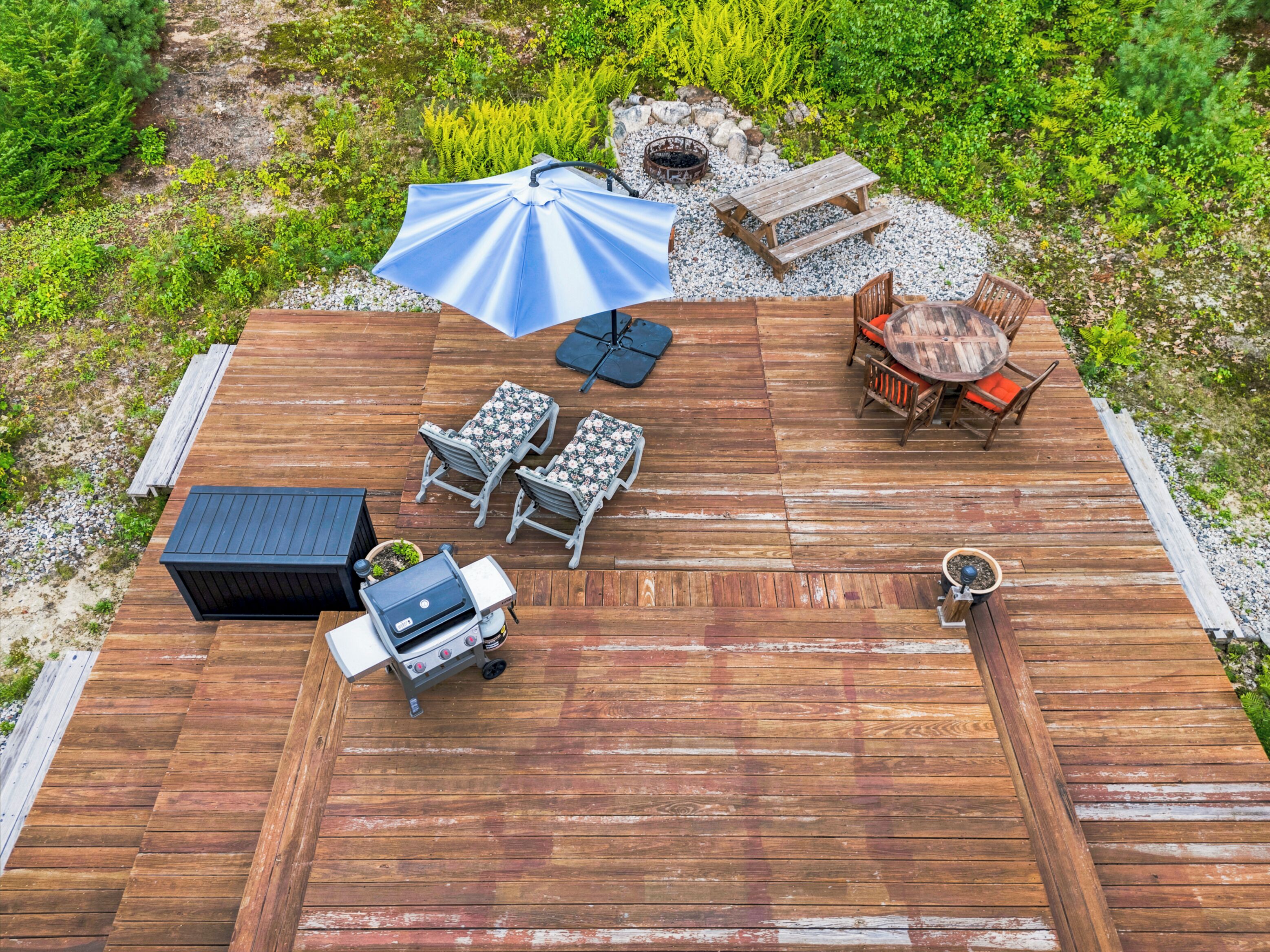 Een houten terras met buitenmeubilair, waaronder een barbecue, tafels en stoelen.