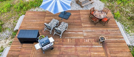 Een houten terras met buitenmeubilair, waaronder een barbecue, tafels en stoelen.