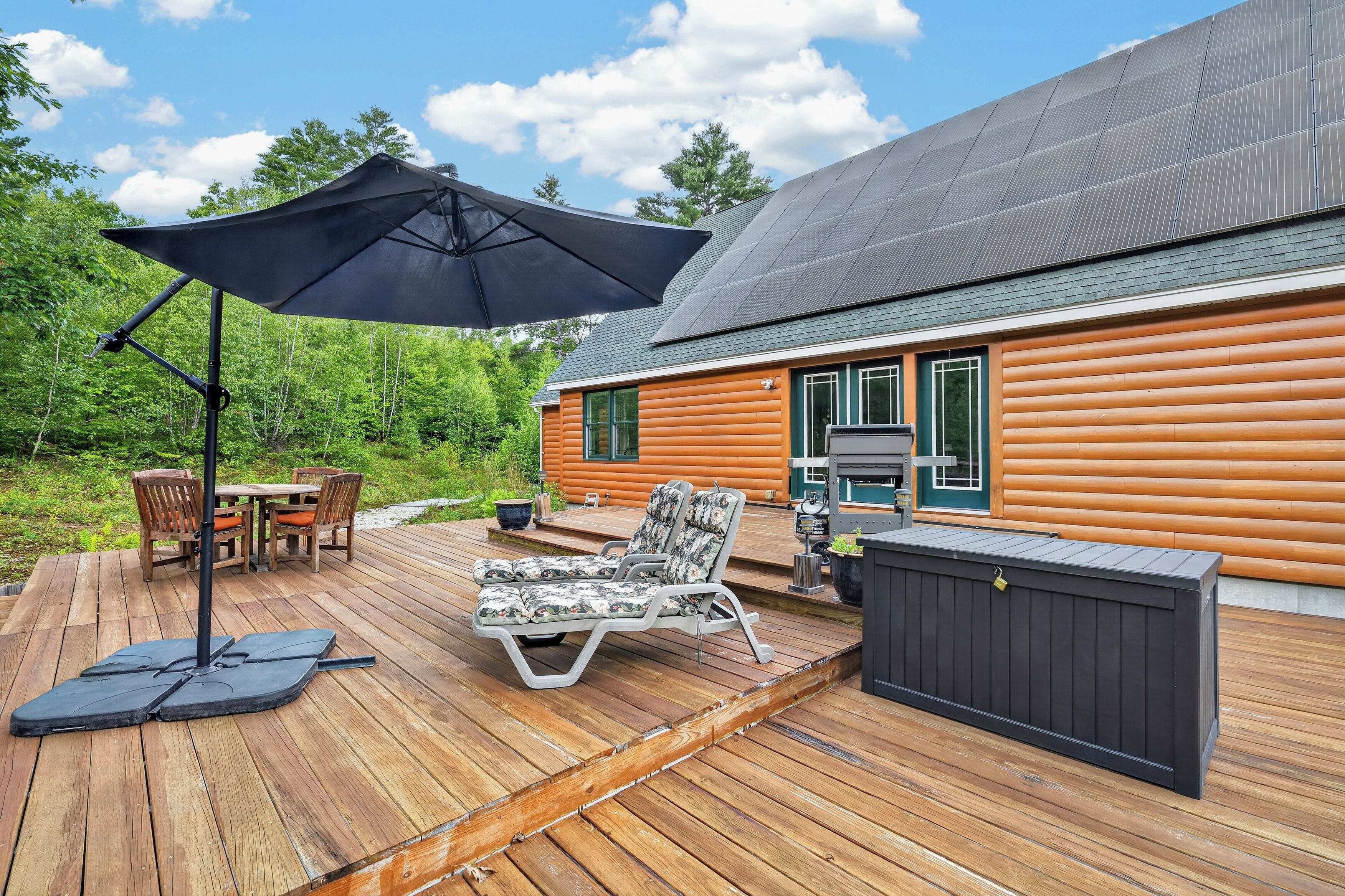 Eine Holzterrasse mit Gartenmöbeln, einem Grill und einem überdachten Bereich mit Sonnenschirm.