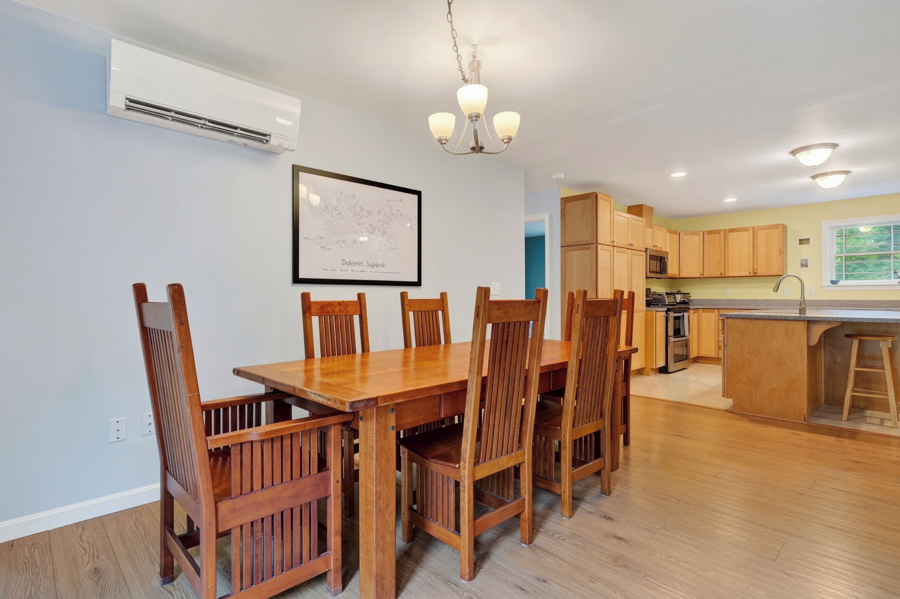 A dining area with a wooden table and chairs, a kitchen with wooden cabinets, and a chandelier.