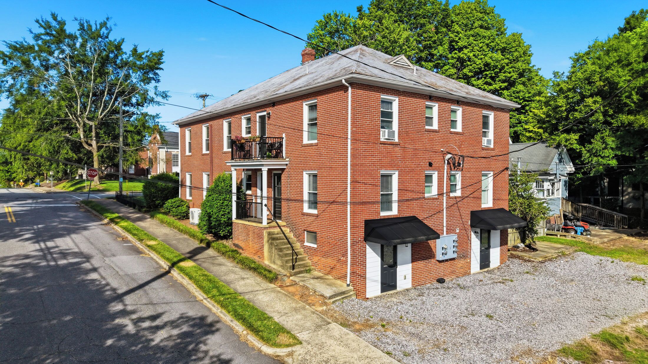 A two-story red brick building with a front porch, a small front yard, and a gravel driveway.