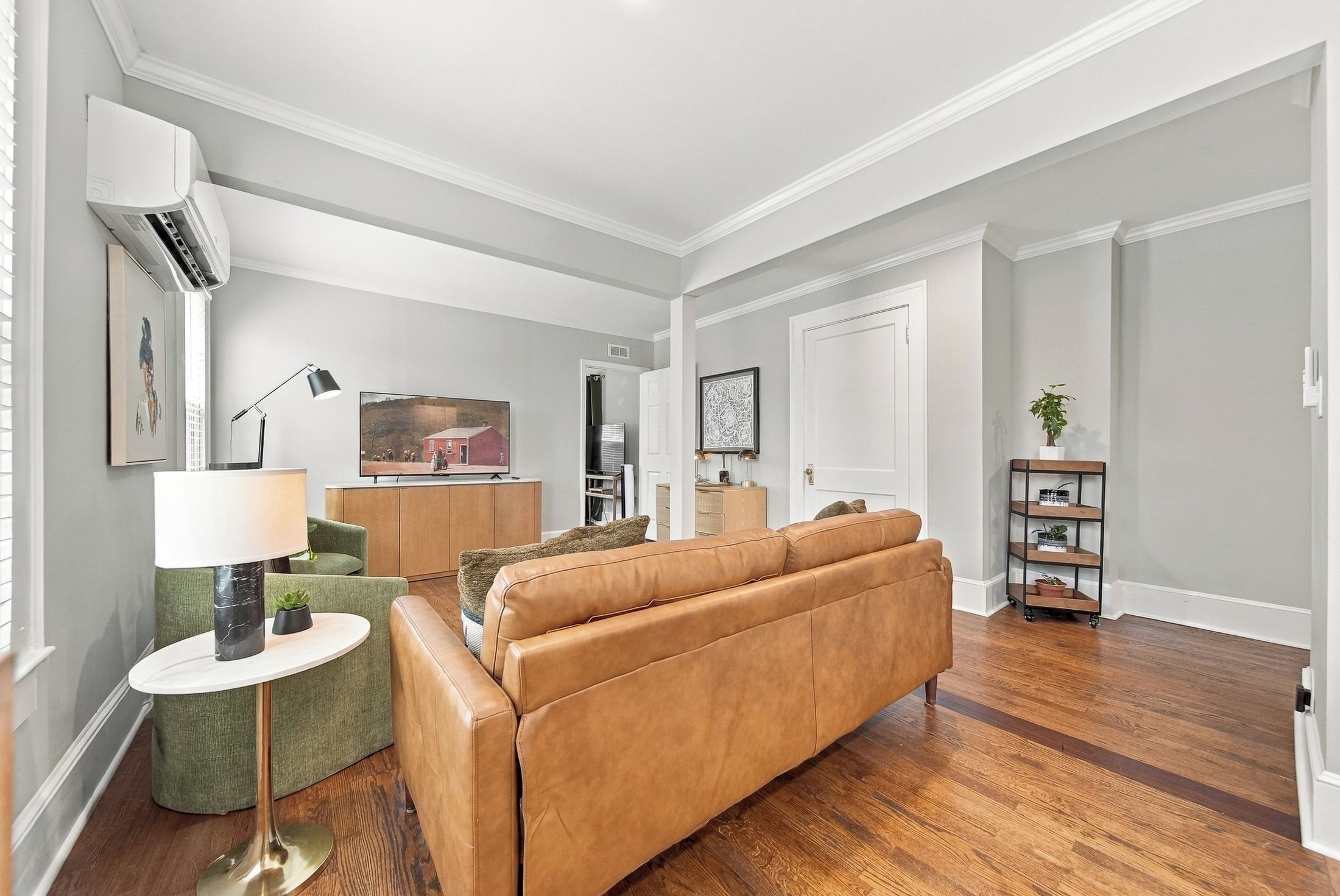A modern living room with a leather sofa, a green armchair, a small table with a lamp, and a television on a stand.