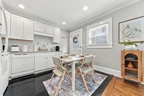 A modern kitchen with white cabinets, a dining table with chairs, and a wooden cabinet with dishes.
