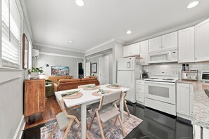A modern kitchen with white cabinets, a dining area with a table and chairs, and a living room with a sofa and a TV. - Downtown Days, Mountain Ways near Lake James (Morganton)