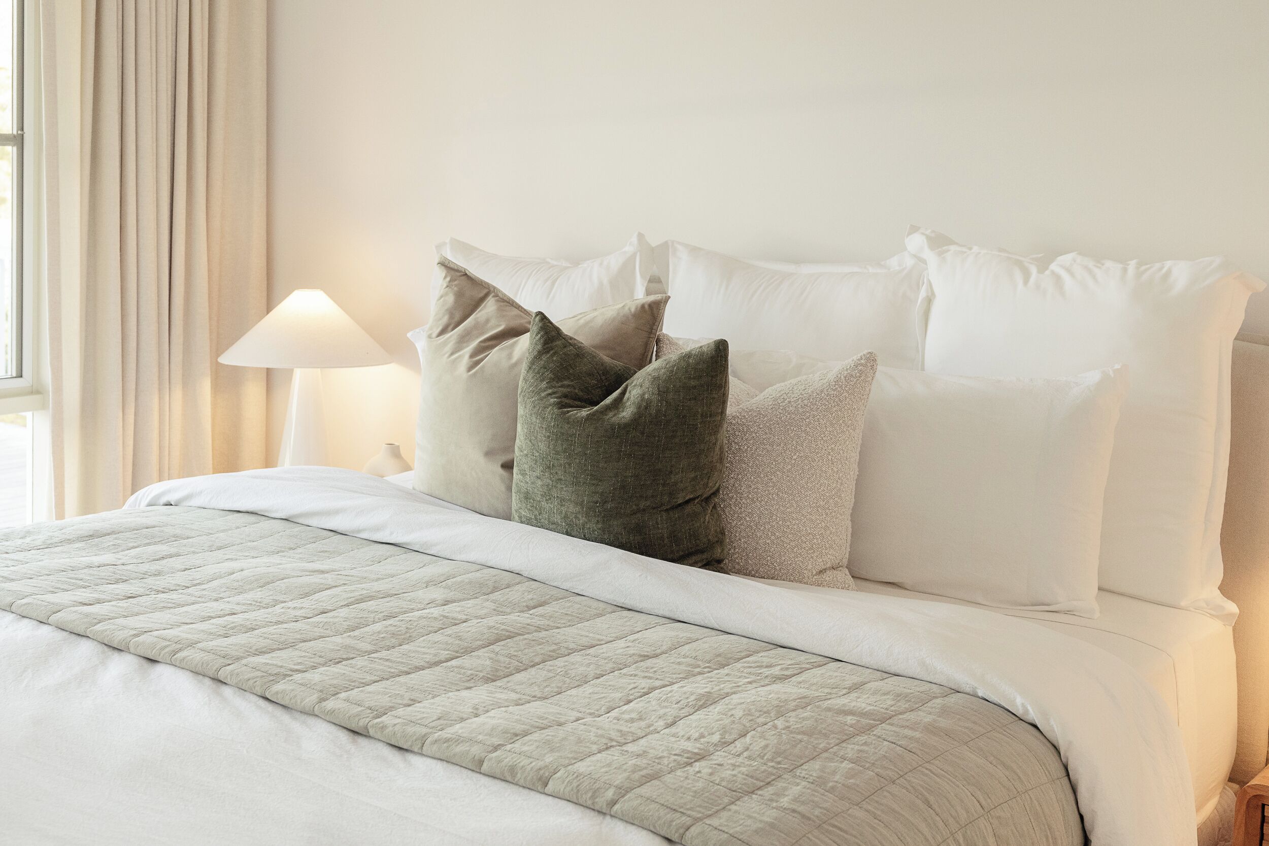 A neatly made bed with a quilted bedspread and a lamp on a bedside table.