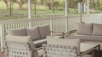 A covered outdoor seating area with a white fence, wooden flooring, and a ceiling fan.