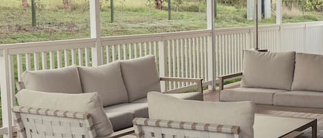 A covered outdoor seating area with a white fence, wooden flooring, and a ceiling fan.