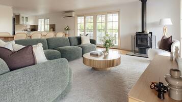 A modern living room with a sectional sofa, a round wooden coffee table, and a black wood-burning stove.